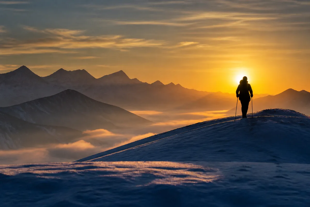 Silhouette d’un randonneur de dos progressant sur une crête enneigée à contre-jour